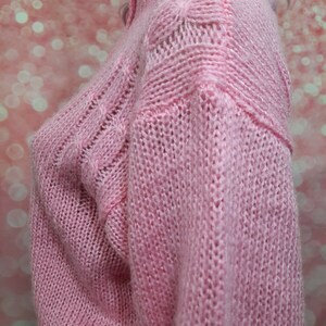 May include: A pink knitted sweater with a cable knit pattern. The sweater has a high neck and long sleeves.