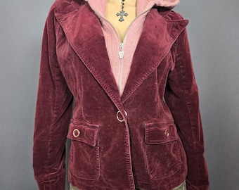 May include: Burgundy velvet blazer with a large collar, two front pockets, and a single button closure. A light pink hooded sweater is visible underneath. The blazer has a classic, tailored design.