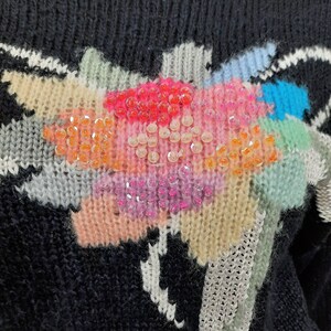 May include: A black knitted sweater with a colorful abstract design featuring sequins. The design includes shades of pink, blue, green, and orange.