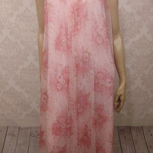 Pode incluir: Uma camisola rosa vintage com um padr&atilde;o floral. A camisola apresenta um tecido transparente e fluido com uma delicada estampa floral em tons de rosa e bege. Possui mangas curtas e uma borda de renda ao redor do decote.