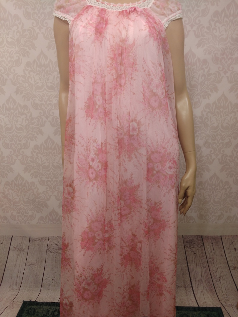 Pode incluir: Uma camisola rosa vintage com um padr&atilde;o floral. A camisola apresenta um tecido transparente e fluido com uma delicada estampa floral em tons de rosa e bege. Possui mangas curtas e uma borda de renda ao redor do decote.