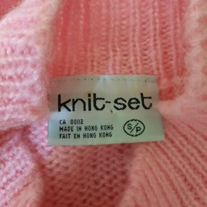 May include: A pink knit sweater with a white tag that reads "knit-set" and "CA 00112 MADE IN HONG KONG FAIT EN HONG KONG".