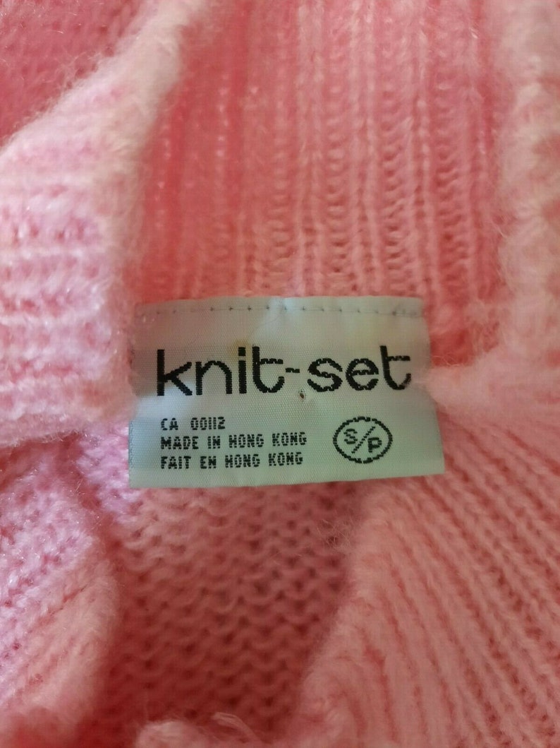 May include: A pink knit sweater with a white tag that reads "knit-set" and "CA 00112 MADE IN HONG KONG FAIT EN HONG KONG".