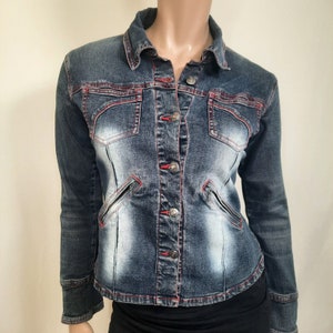 May include: A blue denim jacket with red stitching and silver buttons. The jacket has a faded look and two pockets on the chest.