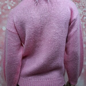 May include: A pink knitted sweater with long sleeves and a turtleneck.