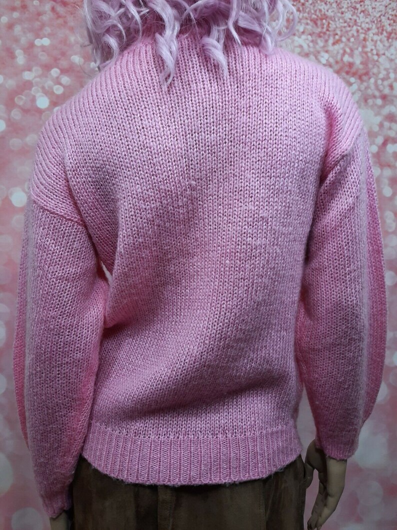 May include: A pink knitted sweater with long sleeves and a turtleneck.