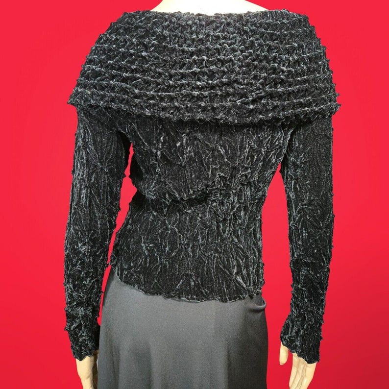 May include: Black long-sleeved top with a ruffled neckline and a textured, crinkled fabric.