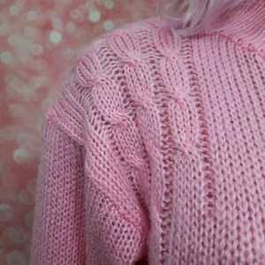May include: A pink knitted sweater with a cable knit pattern.