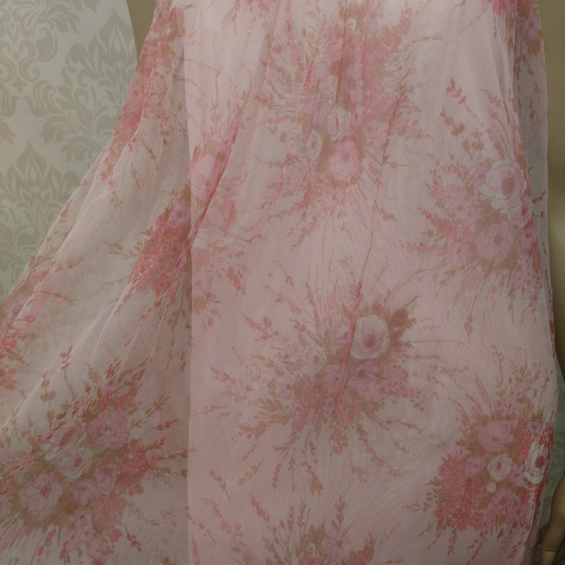 Pode incluir: Um tecido transparente rosa claro com um padr&atilde;o floral em tons de rosa e castanho. O design apresenta bouquets de rosas e outras flores, criando uma est&eacute;tica delicada e rom&acirc;ntica. O tecido parece leve e fluido.