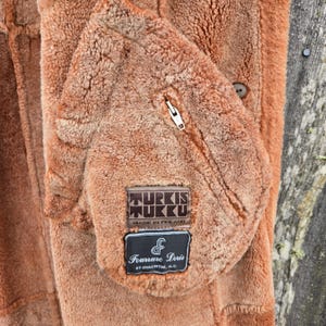 May include: A brown sheepskin jacket with a zipper closure and two leather patches. The patches are labeled "Turkis Tukku Made in Finland" and "Fourrure Doris St-Hyacinthe, Q.C."