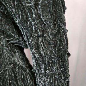 May include: Close-up of a dark green velvet fabric with a textured, crinkled pattern.