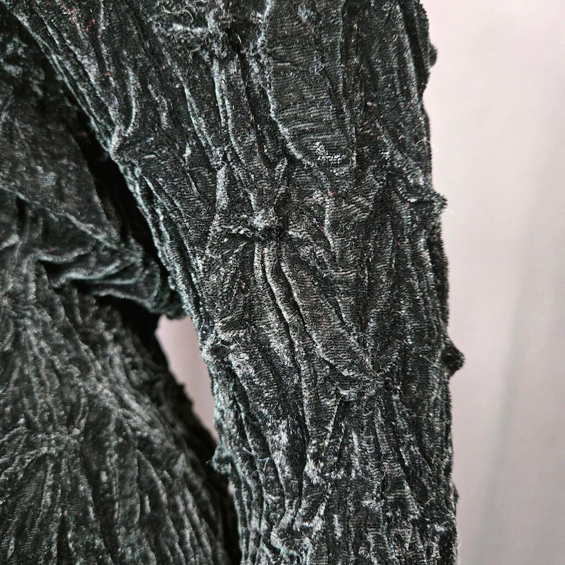 May include: Close-up of a dark green velvet fabric with a textured, crinkled pattern.