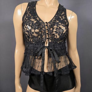 May include: Black lace top with a V-neckline, button closure, and a ribbon tie at the waist. The top features a delicate floral lace pattern and a sheer, layered design. The garment is sleeveless and has a peplum-style hem.