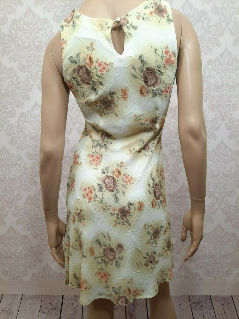 May include: A sleeveless yellow dress with a floral print featuring brown and orange roses. The dress has a keyhole opening at the back of the neckline.