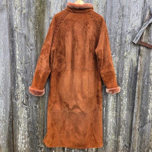 May include: A long brown suede coat with a fur collar and brown stitching detail on the back.