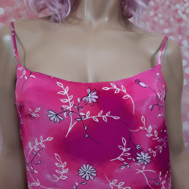 May include: A pink satin camisole with a floral print. The print features white flowers and leaves on a pink background.