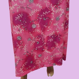 May include: Pink maxi dress with a white floral pattern. The dress has a tie at the waist and a flowing skirt.