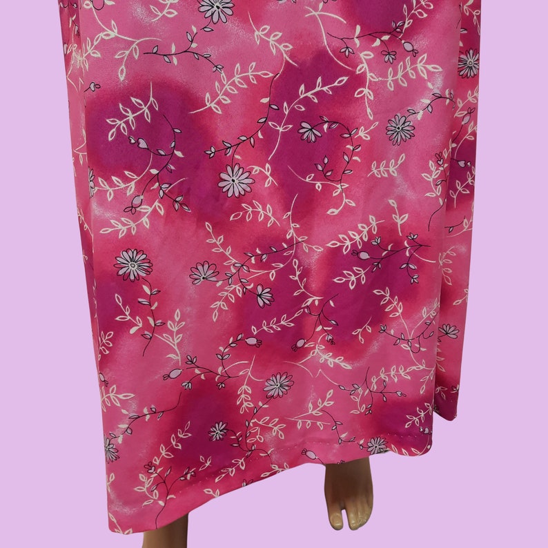 May include: Pink maxi dress with a white floral pattern. The dress has a tie at the waist and a flowing skirt.