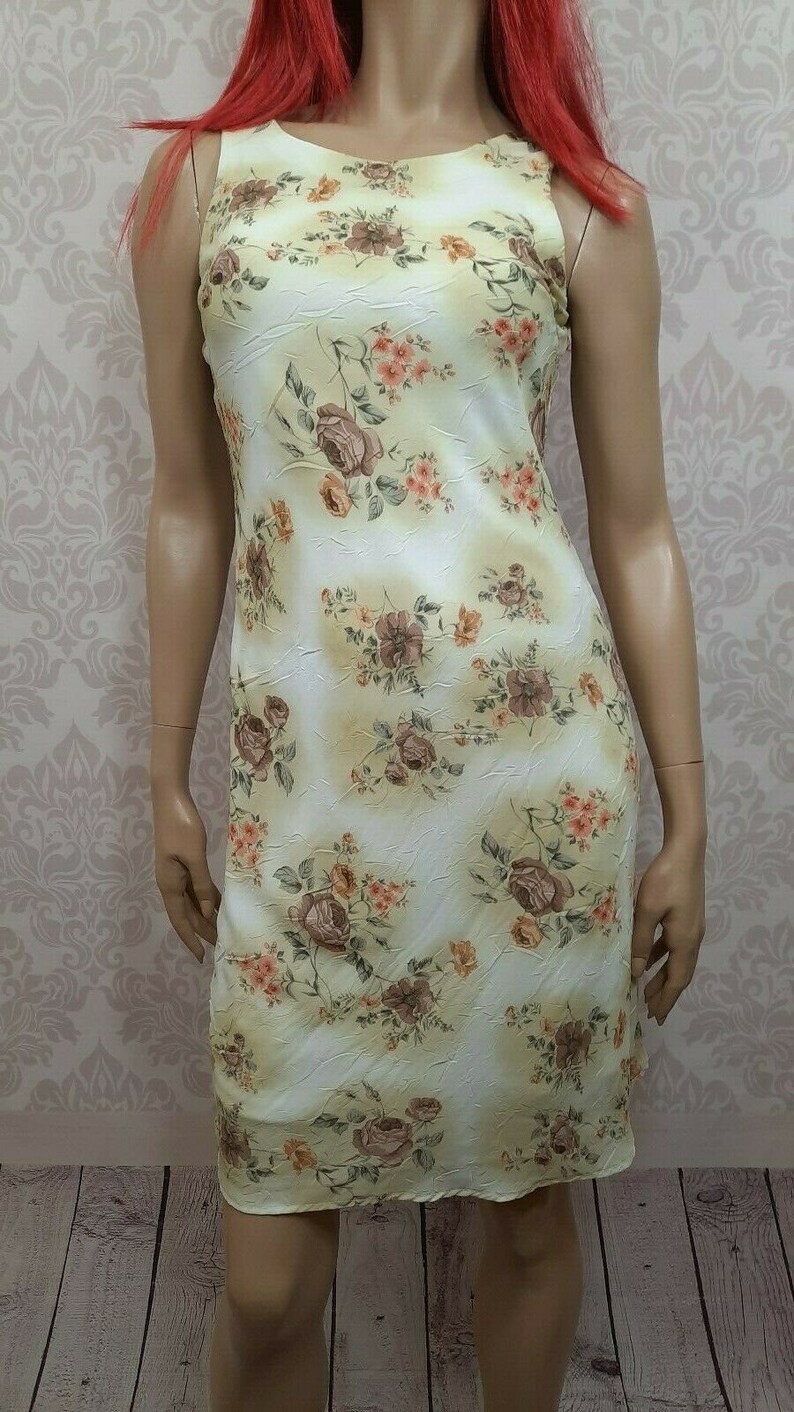 May include: A sleeveless dress with a floral print in shades of brown, pink, and yellow on a white background. The dress has a scoop neck and a fitted silhouette.