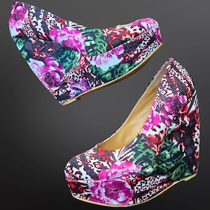May include: A pair of platform wedge heels with a vibrant floral and animal print design. The heels feature a mix of pink, purple, green, and black patterns, creating a bold and eye-catching look. The inner sole is a light tan color.