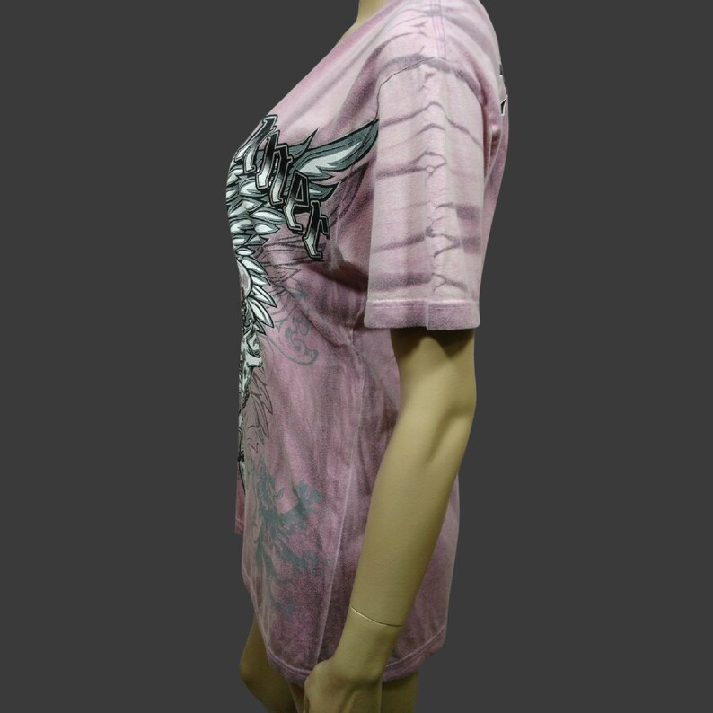 May include: A pink tie-dye t-shirt with a black and white graphic print of an angel with wings. The graphic includes the text "Angel"