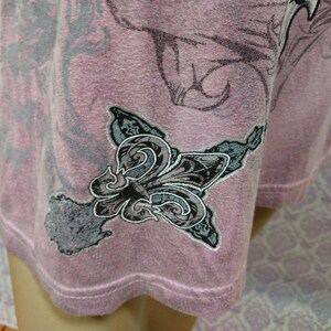 May include: A pink t-shirt with a gray and black floral design. The design includes a fleur-de-lis.