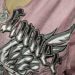 May include: A pink t-shirt with a graphic print of a stylized wing and the word "RIDER" in black lettering.