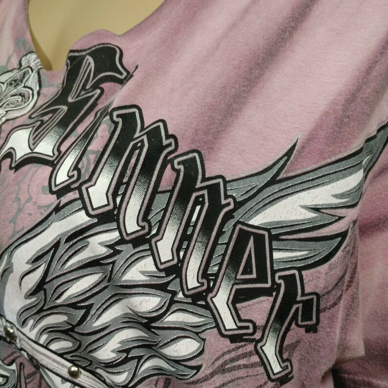May include: A pink t-shirt with a graphic print of a stylized wing and the word "RIDER" in black lettering.