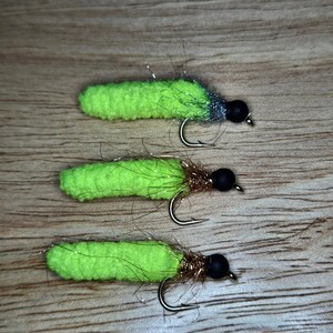 May include: Three lime green fly fishing lures with black and gold accents. The lures are tied on hooks with a black bead at the end.