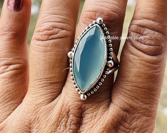 May include: A silver ring with a light blue gemstone set in a marquise shape. The ring is adorned with small silver beads around the gemstone.
