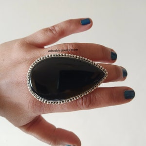May include: A black gemstone ring with a silver setting. The ring is set with a large, oval-shaped black gemstone. The gemstone is surrounded by a silver band with a beaded edge.
