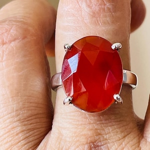 May include: A silver ring with a large, faceted, red gemstone. The ring is on a finger.