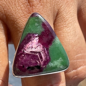 May include: A triangular ring featuring a polished ruby and zoisite gemstone set in a silver-toned metal band. The stone displays a vibrant contrast between deep magenta-red ruby inclusions and opaque green zoisite, with a smooth, flat surface.