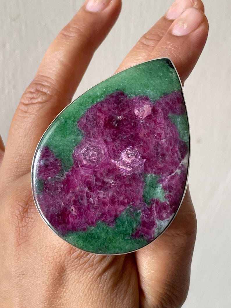 Large teardrop ruby zoisite ring in sterling silver, raw pink-magenta hexagonal ruby crystals set in green zoisite, worn on a hand outdoors.