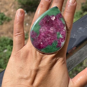 K&ouml;nnte beinhalten: Ein gro&szlig;er tropfenf&ouml;rmiger Ring mit einem polierten Rubin-Zoisit-Edelstein in einer schlichten Fassung aus silberfarbenem Metall. Der Stein zeigt eine lebendige Mischung aus tief magentafarbenen Rubineinschl&uuml;ssen auf einer dunkelgr&uuml;nen Zoisit-Basis.