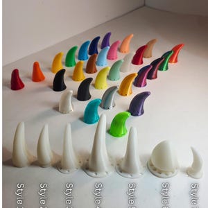 Op de afbeelding: Een verzameling 3D-geprinte hoorns in verschillende kleuren en stijlen. De hoorns vari&euml;ren in grootte en vorm, van kleine kegels tot grotere, gebogen ontwerpen. Elke stijl is voorzien van tekst. Kleuren zijn rood, oranje, geel, groen, blauw, paars en wit.