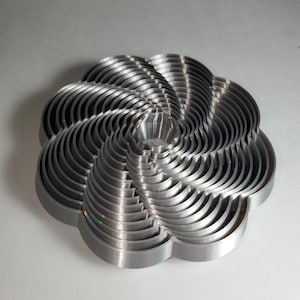May include: A silver metal flower-shaped cookie cutter with multiple layers. The cutter is designed to create a flower-shaped cookie with a spiral pattern.