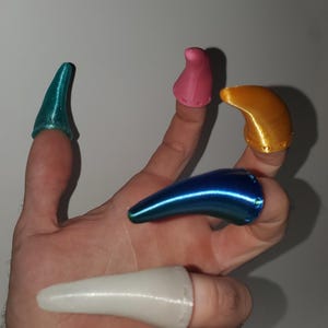 Op de afbeelding: Een hand met zes verschillend gekleurde vingernagels. De nagels zijn in tinten blauw, roze, goud en wit. De nagels zijn gemaakt van een glanzend materiaal en zijn ontworpen om over de vingertoppen te passen.