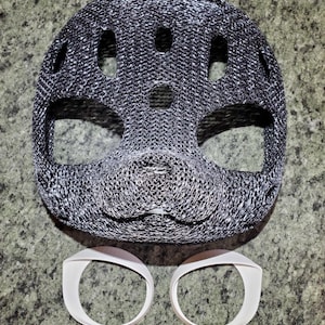 May include: A dark gray, textured, 3D-printed mask with a rounded shape, multiple ventilation holes, and a prominent snout area. Below the mask are two separate, smooth, white, circular plastic rings designed to fit around the eye openings.