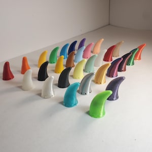 Op de afbeelding: Een verzameling kleine, hoornvormige objecten in verschillende kleuren, waaronder rood, oranje, wit, zwart, geel, groen, blauw, paars, roze en bruin. De objecten zijn gerangschikt op een wit oppervlak.