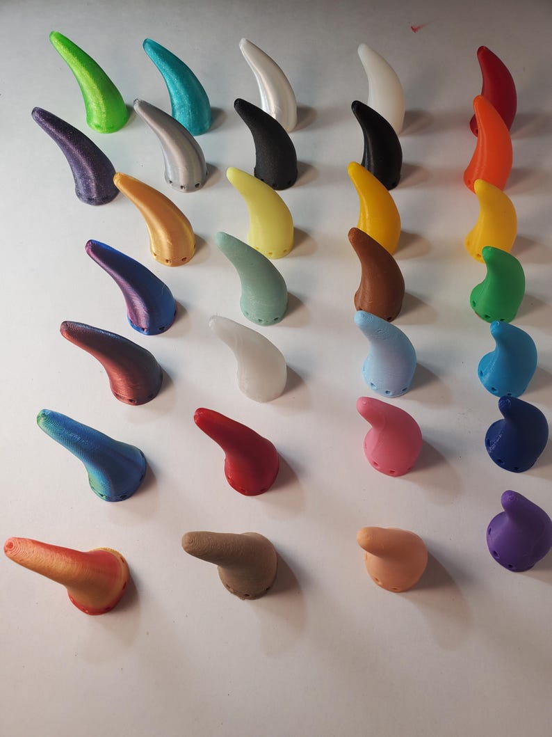 Op de afbeelding: Een verzameling 3D-geprinte hoorns in verschillende kleuren, waaronder groen, blauw, geel en rood. De gebogen hoorns hebben een getextureerd oppervlak. Ze zijn in nette rijen gerangschikt en tonen een verscheidenheid aan tinten en nuances.