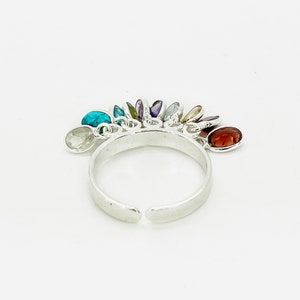 May include: A silver ring with a rainbow of colorful gemstones dangling from it. The ring is open and adjustable.