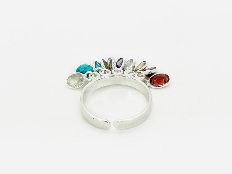 May include: A silver ring with a rainbow of colorful gemstones dangling from it. The ring is open and adjustable.