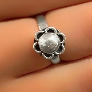 May include: A silver ring with a flower-shaped design. The center of the flower is a round, slightly textured piece of metal.