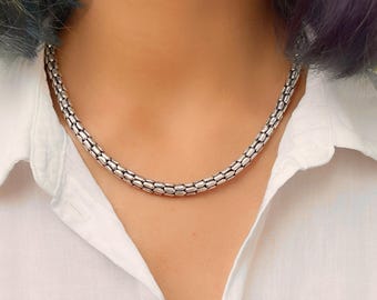 Puede incluir: Un collar de cadena de plata con un diseño delicado y enlazado. El collar está hecho de pequeños eslabones ovalados que están conectados entre sí para crear una cadena lisa y continua.