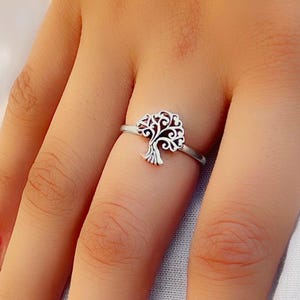 May include: A silver ring with a tree of life design. The ring is on a person's finger.