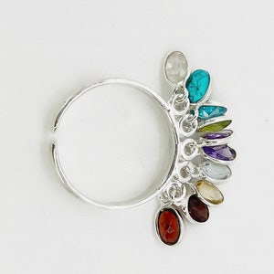 May include: A silver adjustable ring with a rainbow of colorful gemstones dangling from it. The gemstones are in a variety of shapes and sizes, and they are all set in silver.