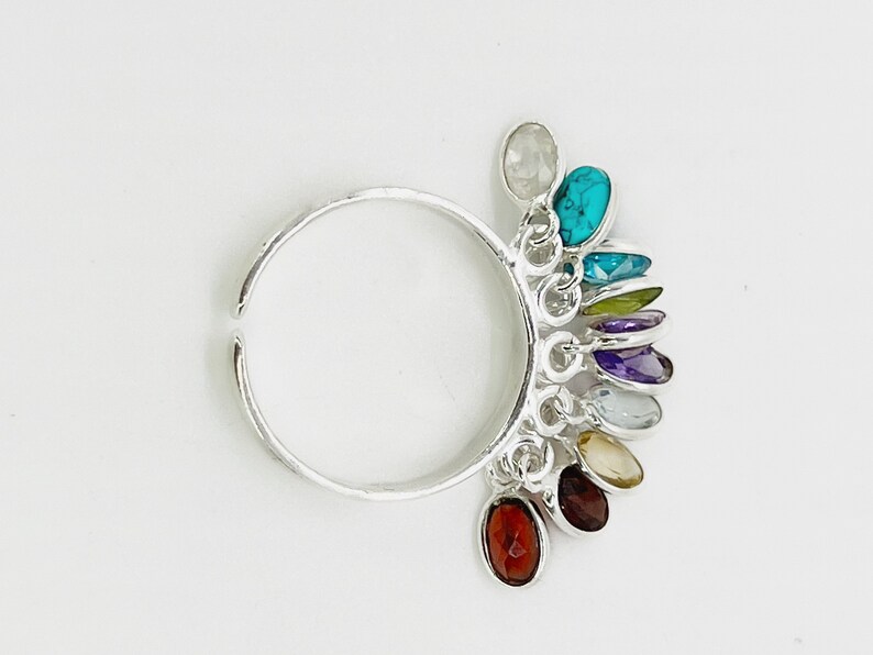 May include: A silver adjustable ring with a rainbow of colorful gemstones dangling from it. The gemstones are in a variety of shapes and sizes, and they are all set in silver.