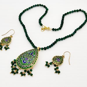 May include: A green gemstone necklace with a matching pair of earrings. The pendant and earrings feature a gold-toned teardrop design with intricate blue and green enamel work.