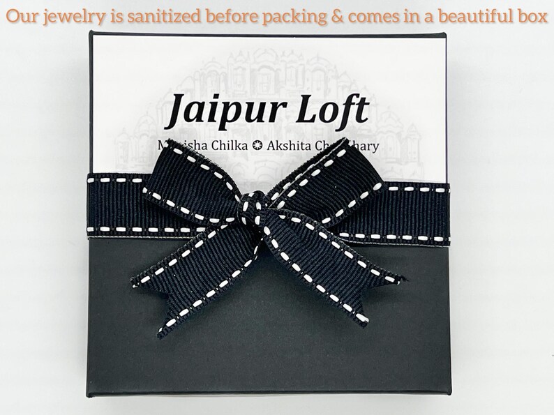 May include: A black gift box with a black ribbon tied in a bow. The box has a white label with the text "Jaipur Loft" and the names "Misha Chilka" and "Akshita Chhary".